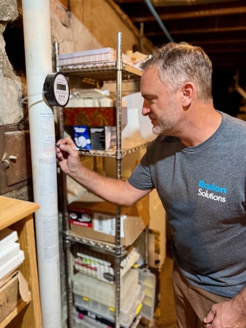 Technician Inspecting Radon Mitigation System in Basement
